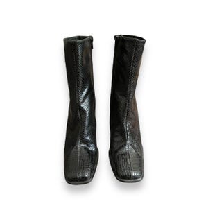 May include: A pair of black ankle boots with a snakeskin pattern. The boots have a square toe and a low heel.