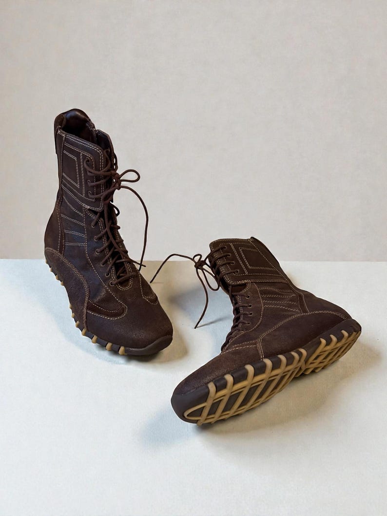 May include: A pair of brown leather boots with a high-top design. The boots feature a lace-up closure, visible stitching, and a tan rubber sole. The boots are designed for casual wear.
