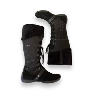 May include: A pair of black knee-high boots with a lace-up front and a zipper on the back. The boots have a black suede toe and heel. The boots are labeled "esprit" on the side.