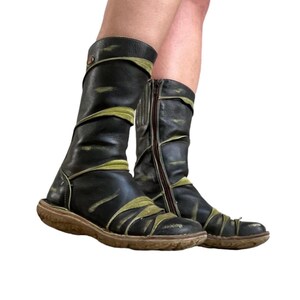 May include: A pair of black leather boots with olive green accents. The boots have a side zipper and a round toe. The soles are brown. The boots appear to be worn.