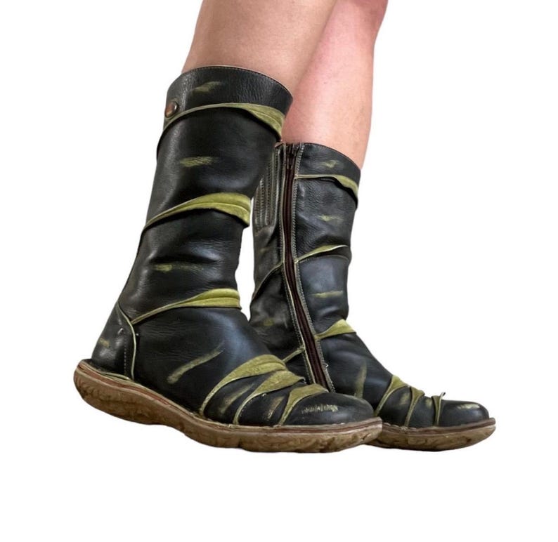 May include: A pair of black leather boots with olive green accents. The boots have a side zipper and a round toe. The soles are brown. The boots appear to be worn.