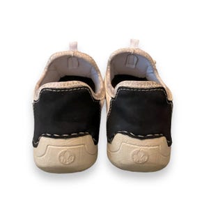 May include: A pair of white canvas slip-on shoes with black suede accents and a white logo on the sole.