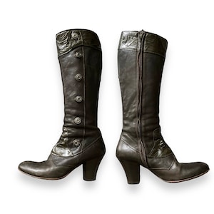 May include: A pair of dark brown leather knee-high boots with a chunky heel. The boots have a zipper on the back and a button closure on the side.