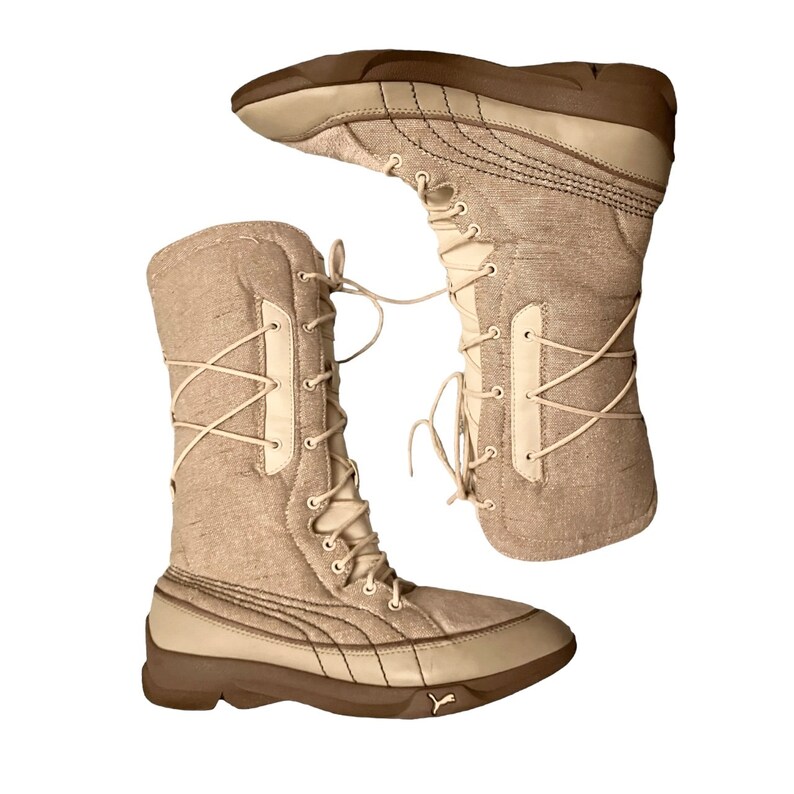 May include: A pair of beige winter boots with a lace-up front and a brown rubber sole. The boots are made of a textured fabric and have a white leather trim.