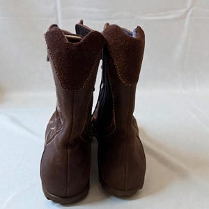 May include: A pair of brown suede boots with a zipper closure. The boots have a rounded toe and a short heel. The top of the boot has a suede collar. The boots are displayed against a white background.