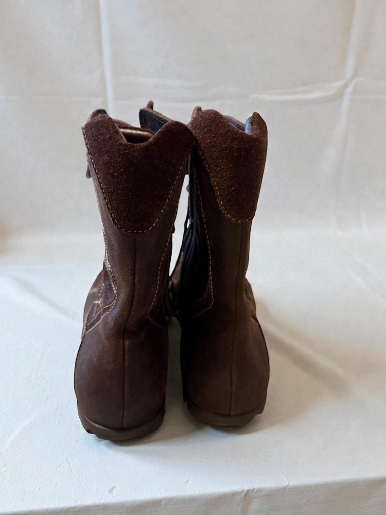 May include: A pair of brown suede boots with a zipper closure. The boots have a rounded toe and a short heel. The top of the boot has a suede collar. The boots are displayed against a white background.
