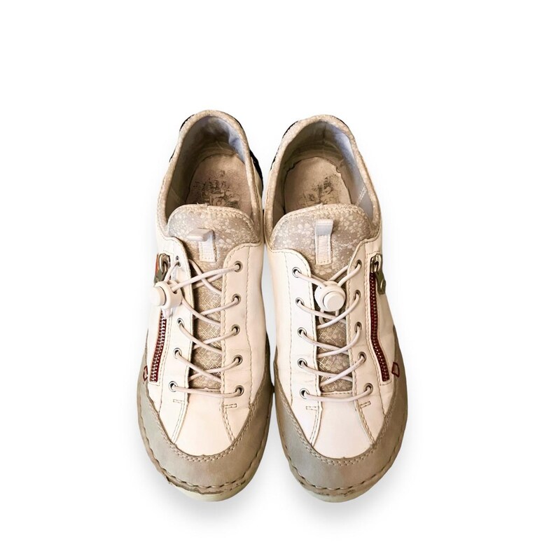 May include: White leather sneakers with a zipper detail on the side. The laces are tied and the shoes have a light brown sole.
