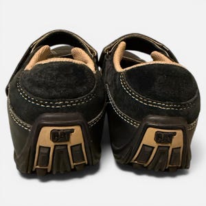 May include: Pair of black suede Caterpillar shoes with tan accents. The shoes have a hook-and-loop closure and the Caterpillar logo on the heel. The soles are brown and the stitching is white. The shoes are designed for casual wear.