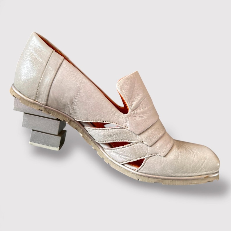 May include: A pair of off-white leather heeled shoes with cutouts and a stacked heel.