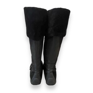 May include: A pair of black knee-high boots with a faux fur cuff. The boots have a zipper on the inside of the ankle and a buckle strap across the top of the foot.
