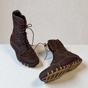 May include: A pair of brown suede boots with a high-top design. The boots feature a lace-up closure, white stitching details, and a tan rubber sole. The boots are designed for casual wear.