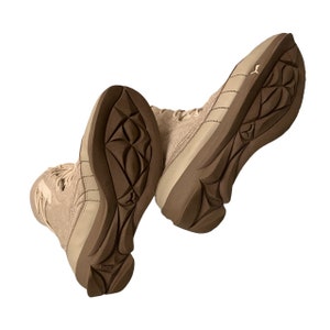 May include: A pair of beige suede boots with brown rubber soles. The boots have a lace-up closure and a chunky heel.