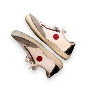 May include: A pair of white leather sneakers with red circle accents and zipper closures.
