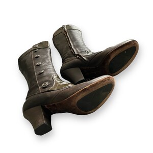May include: A pair of brown leather boots with a chunky heel and a button detail on the shaft. The boots have a pointed toe and a zipper on the back.