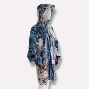 May include: A long-sleeved, hooded raincoat with a blue and white abstract print. The raincoat has a zipper closure and a relaxed fit.