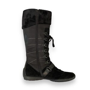 May include: Black suede knee-high boots with a zipper up the back and lace-up detail. The boots have a thick sole and a rounded toe.