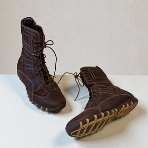 May include: A pair of brown leather boots with a high-top design. The boots feature a lace-up closure, visible stitching, and a tan rubber sole. The boots are designed for casual wear.