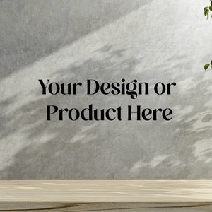 Puede incluir: Una pared de hormigón gris claro con un estante de madera delante. La pared tiene sombras de una ventana u otra fuente de luz. El texto "Your Design or Product Here" está impreso en la pared.