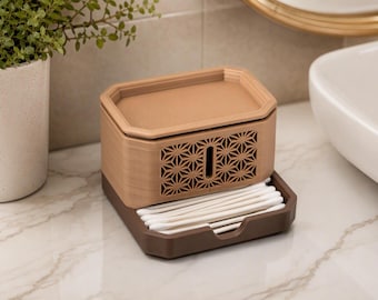 May include: A two-toned rectangular storage container with a light tan top section featuring a geometric star pattern and a vertical slot. The base is a dark brown tray holding a row of white cotton swabs, providing a compact organisation solution.
