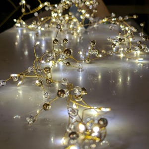 May include: A delicate, gold-toned hair vine with clear and brown crystal accents and tiny, warm white LED lights. The flexible wire design allows for versatile styling options for weddings or special occasions.