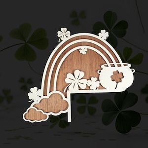 May include: Wooden St. Patrick's Day decoration with a rainbow, pot of gold, shamrocks, and clouds. The rainbow and clouds are white, with a natural wood background. The pot of gold has a shamrock cutout.