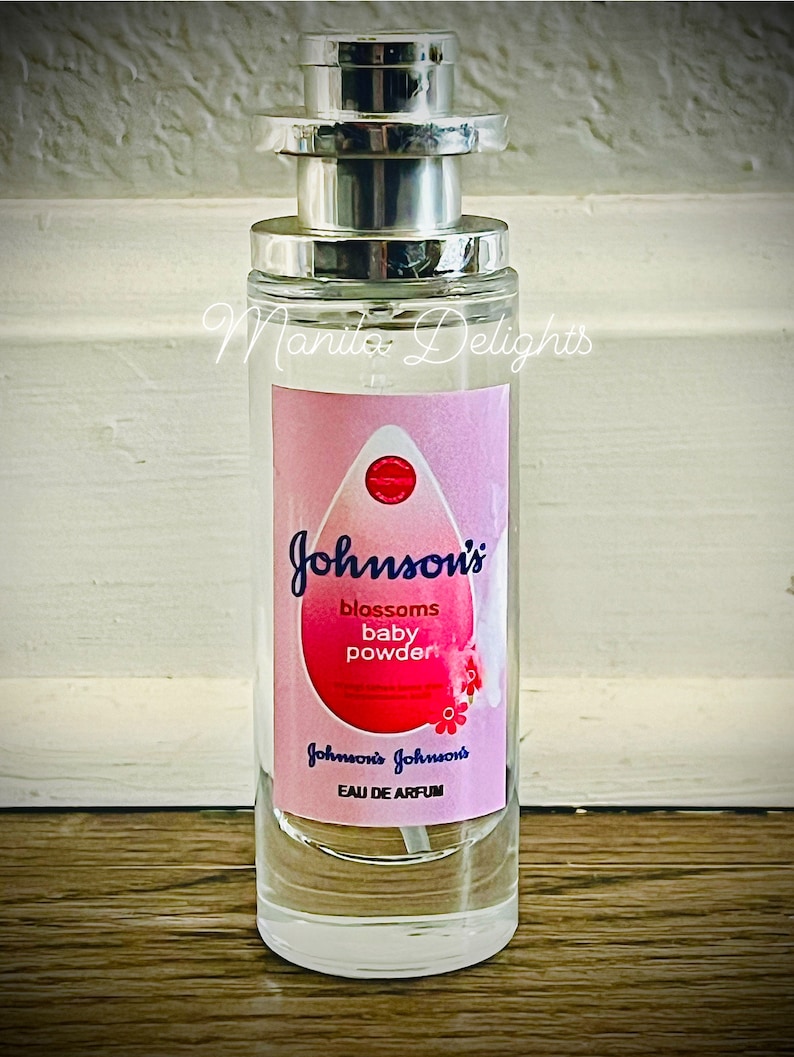 May include: A clear glass bottle with a silver spray nozzle and a pink and white label. The label says "Johnson's blossoms baby powder" and "Johnson's Johnson's Eau de Parfum".