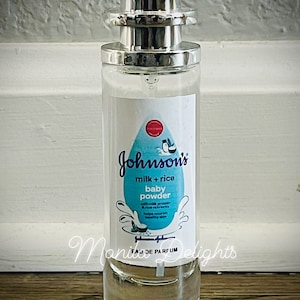May include: A clear glass bottle of Johnson's milk + rice baby powder perfume. The bottle has a silver cap and a white label with blue text and a blue and white illustration of a coconut.