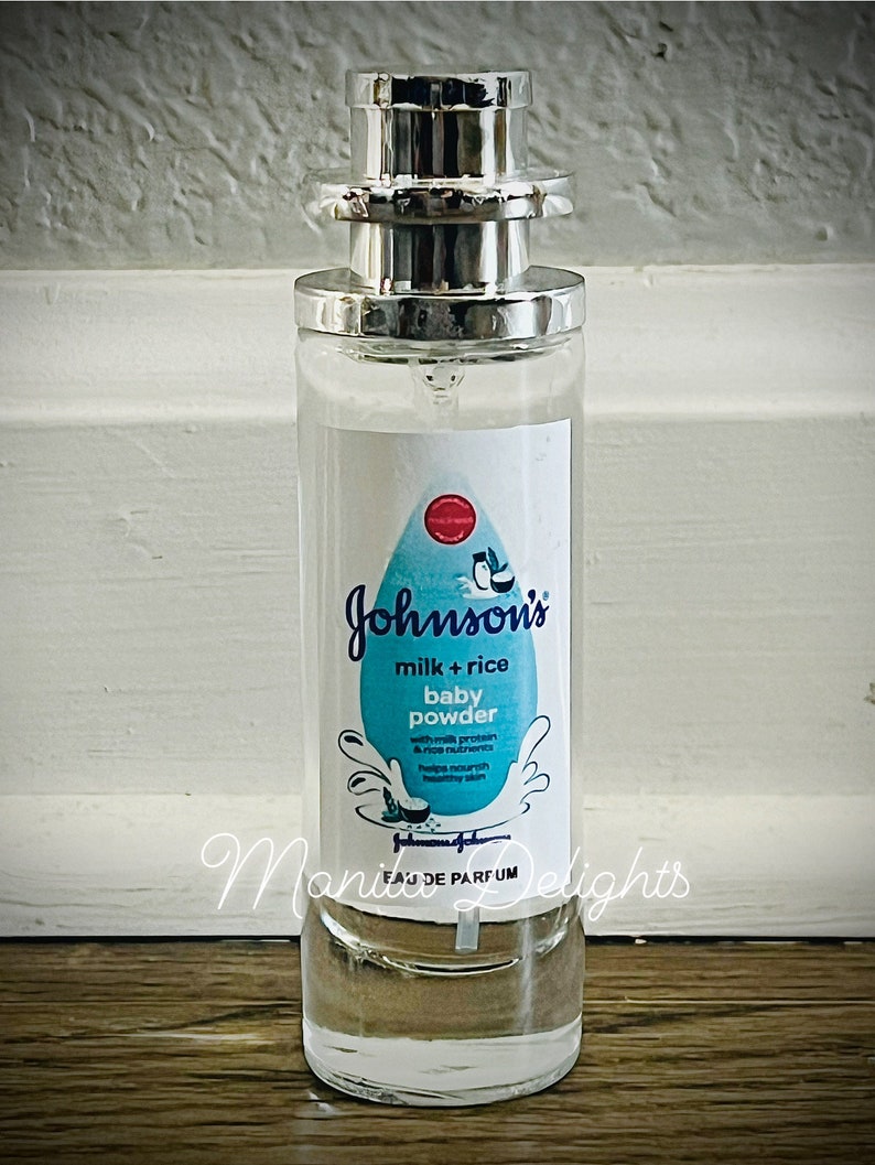 May include: A clear glass bottle of Johnson's milk + rice baby powder perfume. The bottle has a silver cap and a white label with blue text and a blue and white illustration of a coconut.