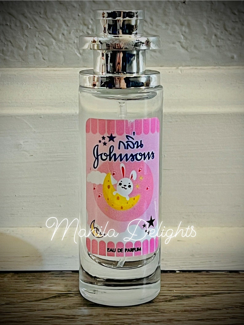 May include: A clear glass bottle of Johnson's baby perfume with a pink label featuring a white bunny on a yellow moon. The label also has the text "กลิ่น Johnson's" and "Eau de Parfum".