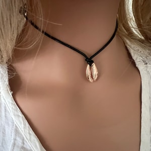 May include: A delicate gold seashell pendant necklace on a black leather cord.