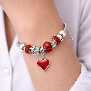 May include: A silver-tone charm bracelet featuring a central red heart pendant, interspersed with red crystal-encrusted beads, smooth silver-tone beads, and a silver-tone barrel charm engraved with the text I LOVE YOU in black lettering.
