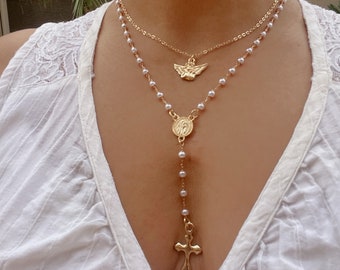 Peut inclure: Un collier en or à plusieurs rangs avec une chaîne de perles, un petit pendentif en forme d'ange et un pendentif plus grand avec une image religieuse. Le collier est également doté d'une croix en or à l'extrémité de la chaîne.