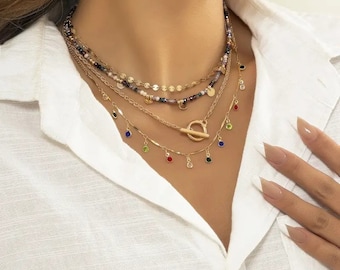 May include: Layered gold necklace with a toggle clasp and colourful gemstone accents. The necklace features a variety of chain styles and beads.