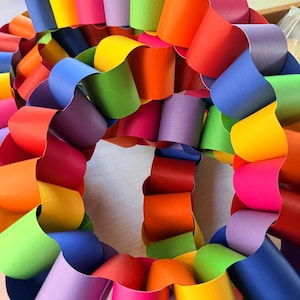 May include: A vibrant, multi-colored paper chain wreath. The wreath is composed of interconnected loops of paper in a rainbow of hues, including red, orange, yellow, green, blue, and purple. The paper is folded and arranged in a circular pattern.