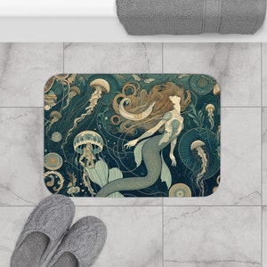 Puede incluir: Una alfombra de baño azul y verde con un diseño de sirena y medusas. La sirena tiene el pelo largo y fluido y una cola con escamas. Las medusas son translúcidas y tienen largos tentáculos.
