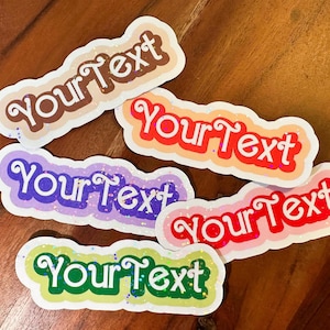 May include: Five colorful stickers with the text "Your Text" in a white cursive font. The stickers are decorated with glitter and have a rounded rectangular shape.