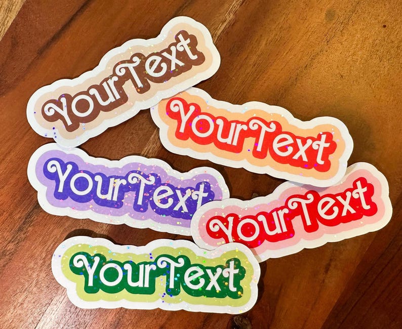 May include: Five colorful stickers with the text "Your Text" in a white cursive font. The stickers are decorated with glitter and have a rounded rectangular shape.