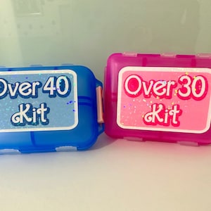 May include: Two pill organizers, one blue and one pink, with labels that say "Over 40 Kit" and "Over 30 Kit".