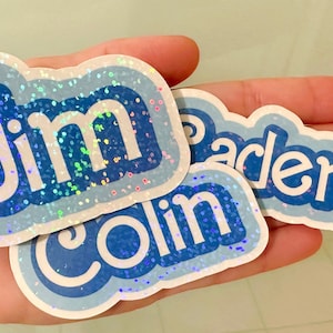 May include: Three blue and white iridescent glitter stickers with the names "Jim", "Colin", and "Jaden" written in white.