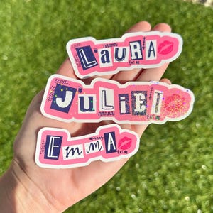 May include: Three pink and white stickers with the names "Laura", "Juliet", and "Emma" written in black letters. Each sticker has a pink lip design and the words "Eat Me" written in black letters.