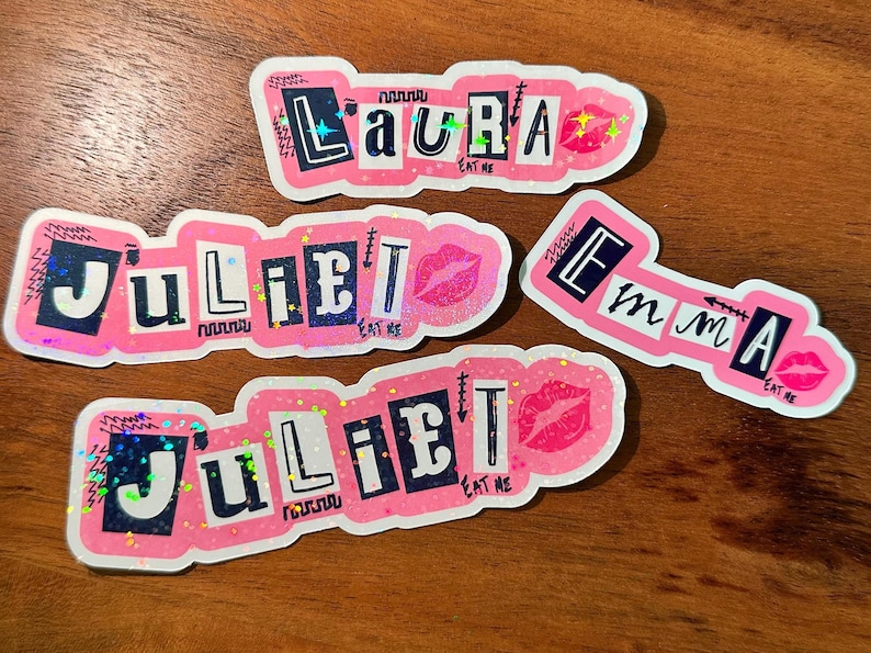 May include: Four pink and white stickers with glitter and black text. The stickers say "Laura Eat Me", "Juliet Eat Me", "Juliet Eat Me", and "Emma Eat Me".