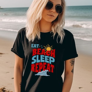 May include: A black t-shirt with a graphic design that says "Eat, Beach, Sleep, Repeat" in red, blue and yellow text with a sun and wave graphic.