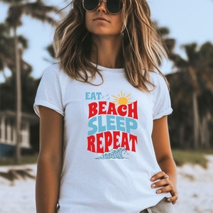 May include: White t-shirt with a graphic design that says "Eat, Beach, Sleep, Repeat" in colourful letters with a sun and waves.