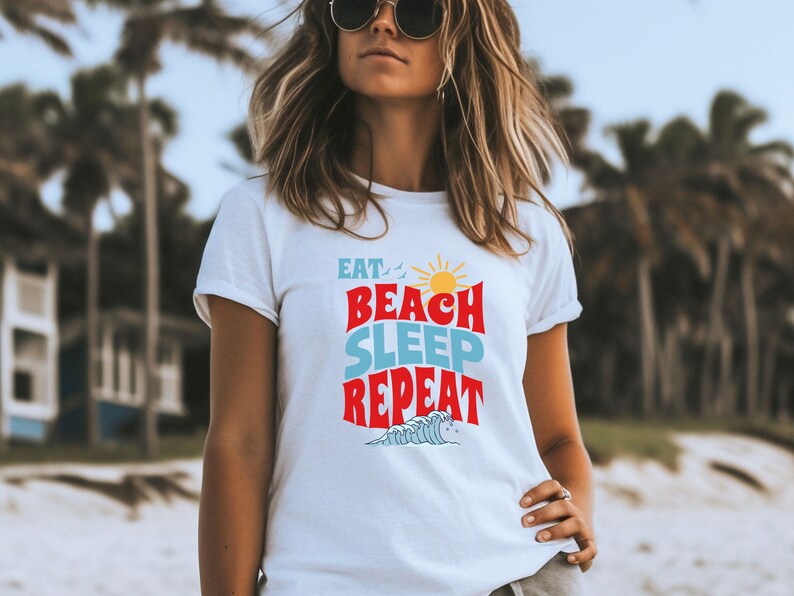 May include: White t-shirt with a graphic design that says "Eat, Beach, Sleep, Repeat" in colourful letters with a sun and waves.