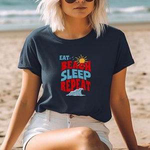 May include: A navy blue t-shirt with a white graphic that says "Eat, Beach, Sleep, Repeat" with a sun and a wave graphic.