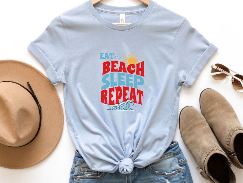 May include: Light blue t-shirt with the text "Eat, Beach, Sleep, Repeat" in red and blue lettering. The shirt features a sun and a wave graphic.
