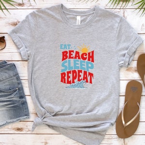 May include: Grey t-shirt with the text "Eat Beach Sleep Repeat" in red, blue and yellow lettering. The text is in a retro font style. A small graphic of a wave is below the text.