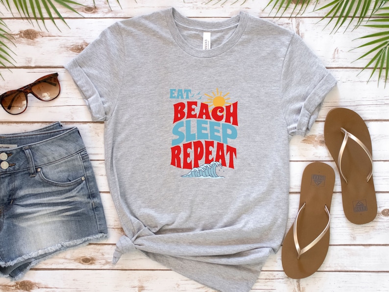 May include: Grey t-shirt with the text "Eat Beach Sleep Repeat" in red, blue and yellow lettering. The text is in a retro font style. A small graphic of a wave is below the text.