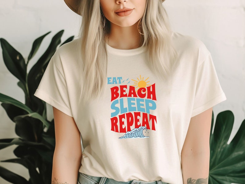 May include: A white t-shirt with a retro-style graphic that says "Eat Beach Sleep Repeat" in red, blue, and yellow. The graphic also includes a sun, birds, and a wave.