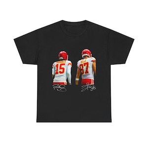 Puede incluir: Camiseta negra con un gráfico de dos jugadores de fútbol americano con uniformes rojos y blancos. Los jugadores llevan cascos rojos y tienen los números 15 y 87 en sus camisetas. También se ven firmas.